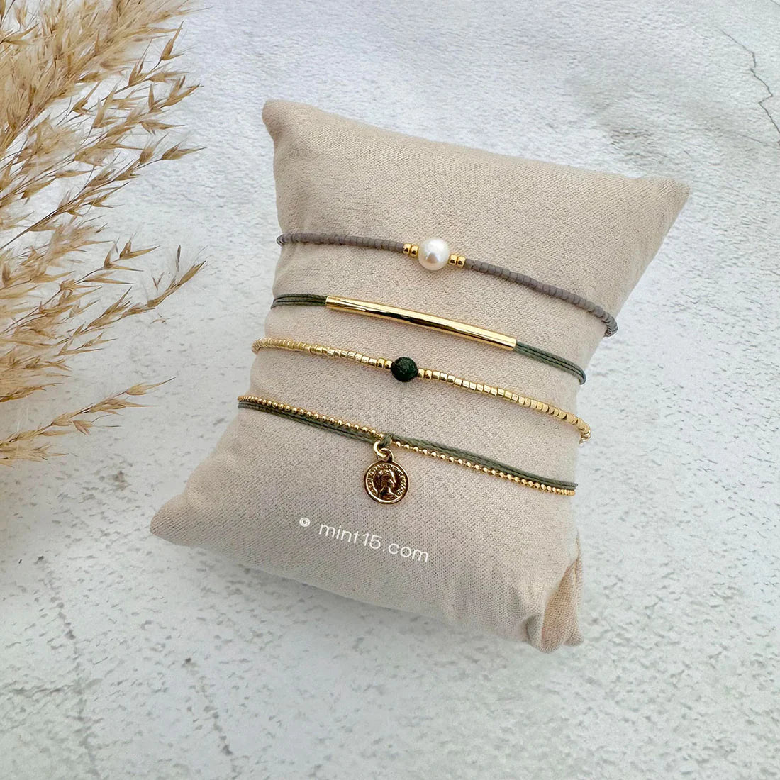Armbanden set army green, goudkleurig, maat 16-19cm, op een sieradenkussentje in wit zand.