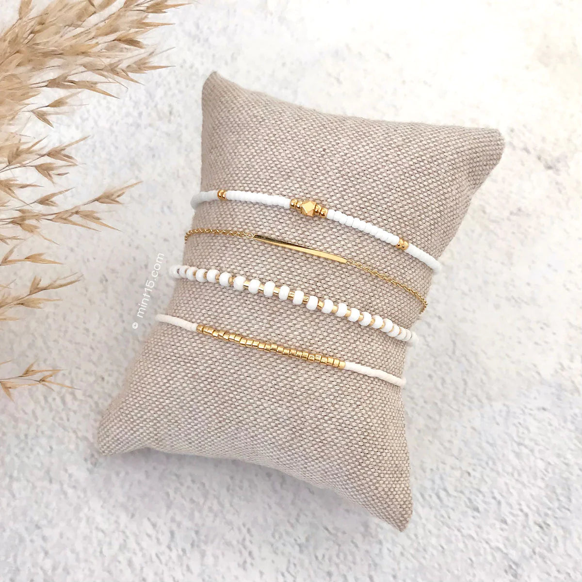 Armbanden set bright white, goudkleurig, maat 16-19cm, op een sieradenkussentje in wit zand.