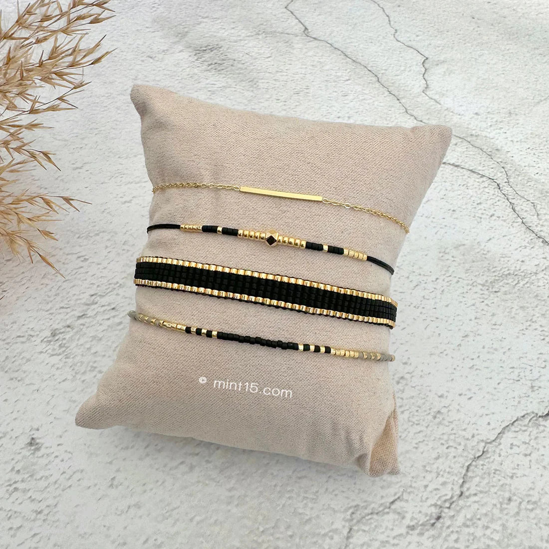 Armbanden set fijn zwart, goudkleurig, maat 16-19cm, op een sieradenkussentje in wit zand.