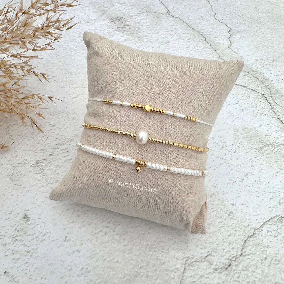Armbanden set pearl shine, goudkleurig, maat 16-19cm, op een sieradenkussentje in wit zand.