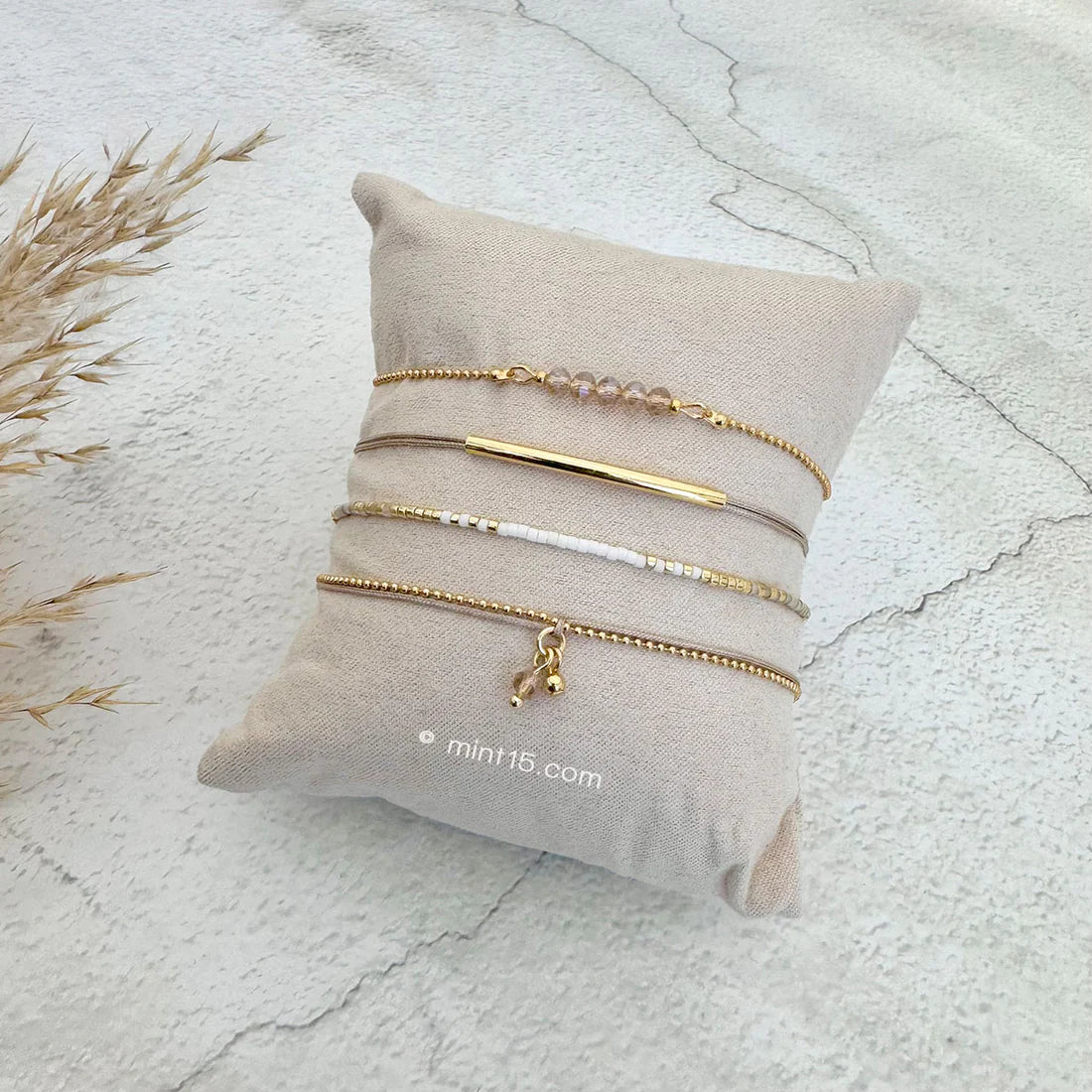 Armbanden set white & natural, goudkleurig, maat 16-19cm, op een sieradenkussentje in wit zand.